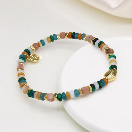 Luxury accessory: Beaded bracelet with multicoloured stones and gold accents, featuring a small gold charm. Perfect for an upmarket event, its beautifully displayed on a white surface.
