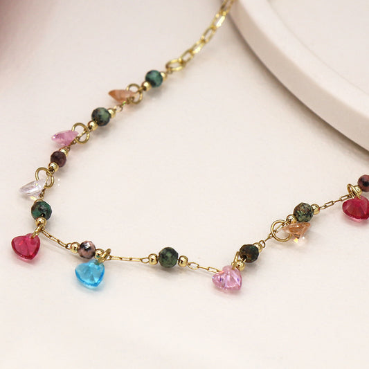 Imitation gold necklace featuring heart-shaped drop pendants and vibrant coloured glass beads on a neutral background.