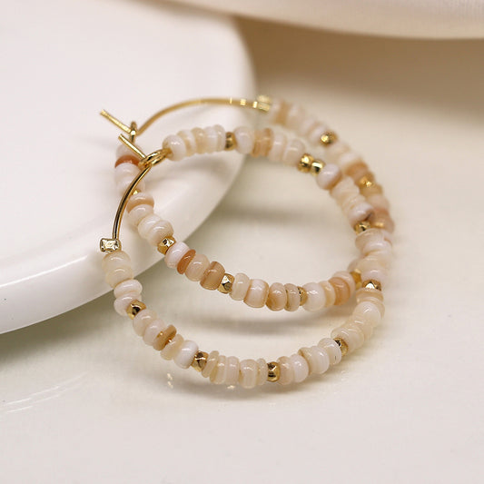 Faux gold-plated hoop earrings embellished with beige and white beads, featuring delicate seed pearls, displayed on a white surface.