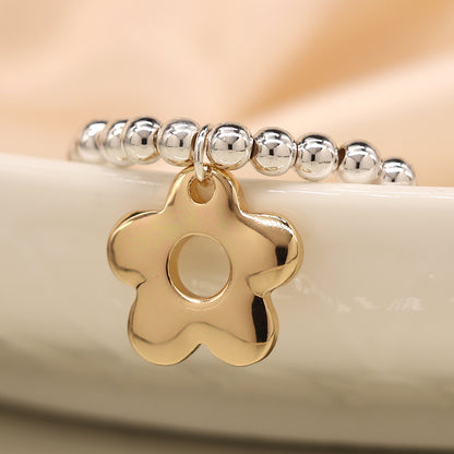 A silver-plated bracelet featuring a retro daisy charm elegantly rests on a white ceramic surface.