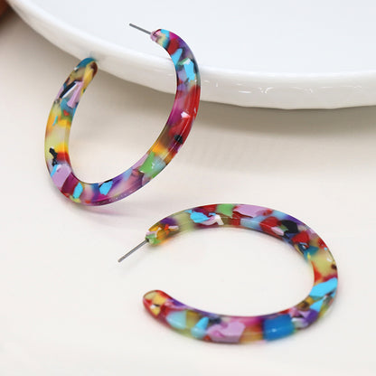 Two colourful terrazzo earrings with multicoloured marbled patterns are displayed on a white surface near a plate, making a vibrant statement piece.