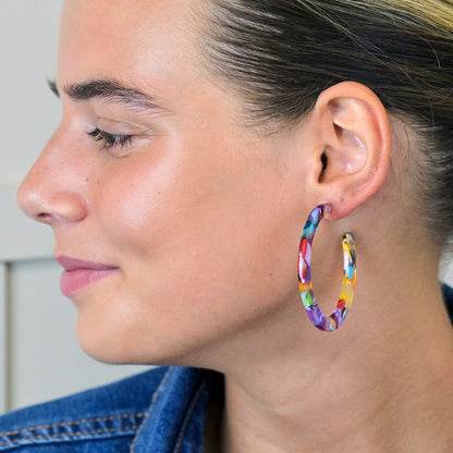 Profile of a person wearing colourful terrazzo earrings, smiling slightly, with hair pulled back, and wearing a blue jacket.