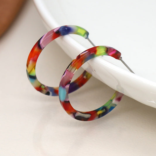 Vibrant multicoloured earrings with a marbled pattern rest on a white dish, capturing attention with their bold statement.