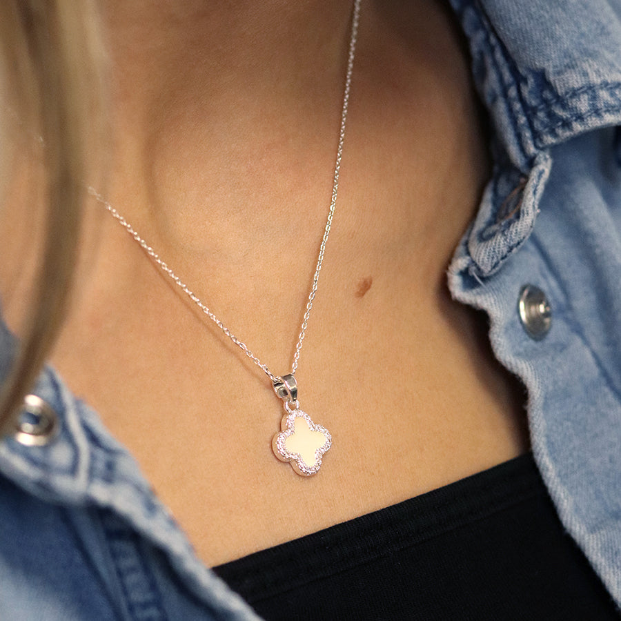 A person wearing a silver-plated necklace with a crystal-edged, clover-shaped pendant. They are dressed in a denim shirt over a black top, showcasing their fine jewellery taste.
