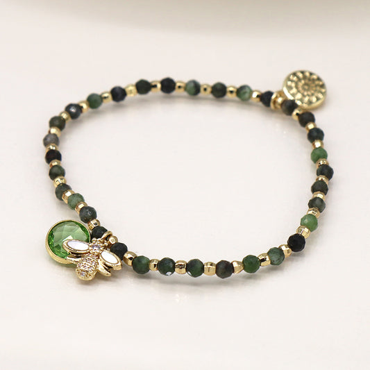 Green & Gold bracelet adorned with a bee charm and circular embellishment lies elegantly on a white surface, showcasing faux gold plated beads.