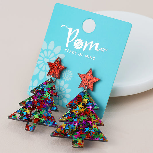 A pair of Christmas tree earrings with multicoloured glitter and red star tops, perfect holiday jewellery, displayed on a blue card labelled “POM Peace of Mind.”.