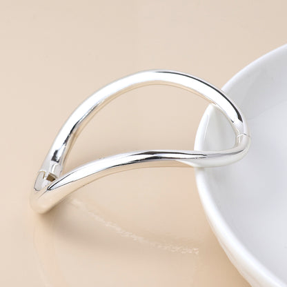 A minimalist, silver-plated bangle rests on the edge of a white dish against a beige background, capturing the essence of modern classic jewellery.