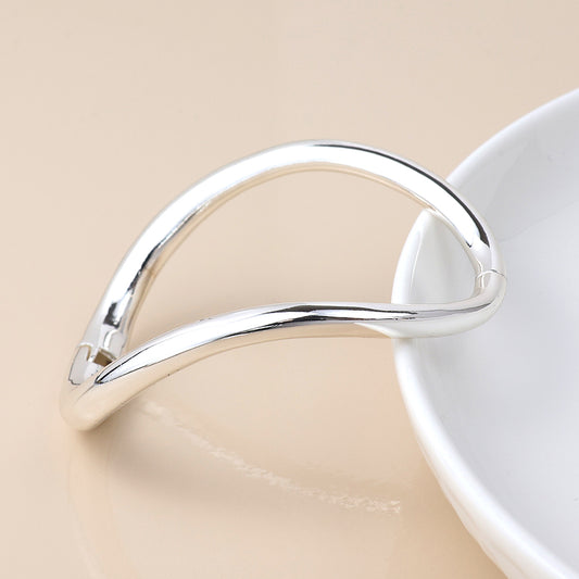 A minimalist, silver-plated bangle rests on the edge of a white dish against a beige background, capturing the essence of modern classic jewellery.