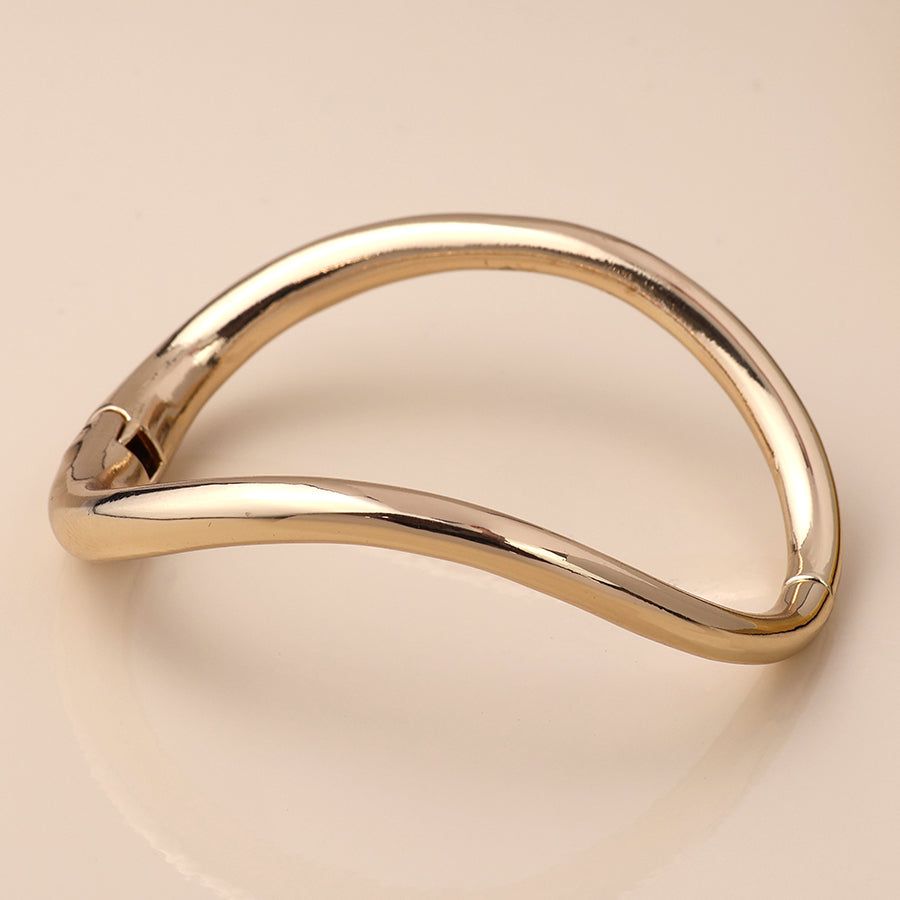 A gold-coloured, asymmetrical stacking bracelet with a smooth, curved design makes for a timeless accessory, elegantly displayed against a light background.