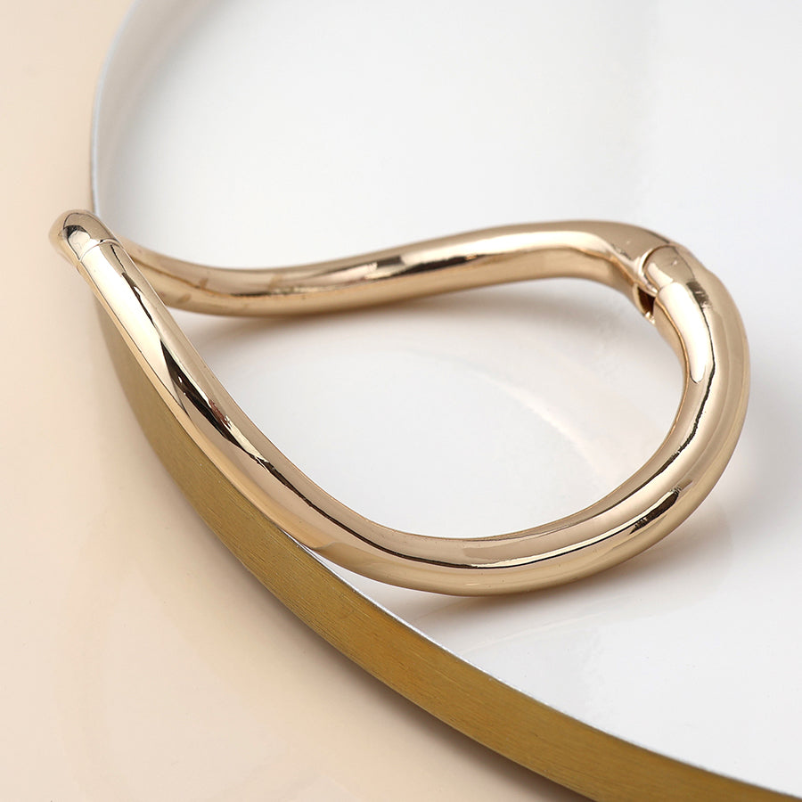 A gold-toned, abstract-shaped stacking bracelet rests on a white and beige surface—a classic accessory for any jewellery collection.