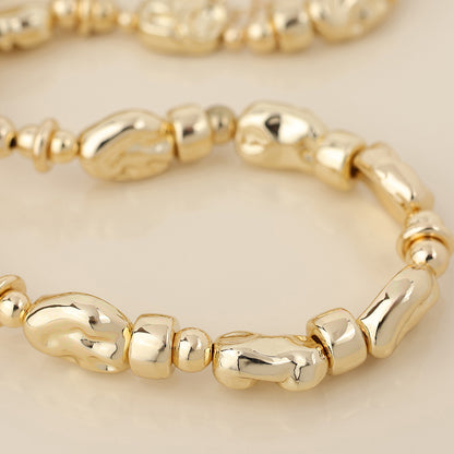 Close-up of a golden bead necklace with irregular, organically shaped beads displayed on a neutral background—an elegant and versatile jewellery piece.