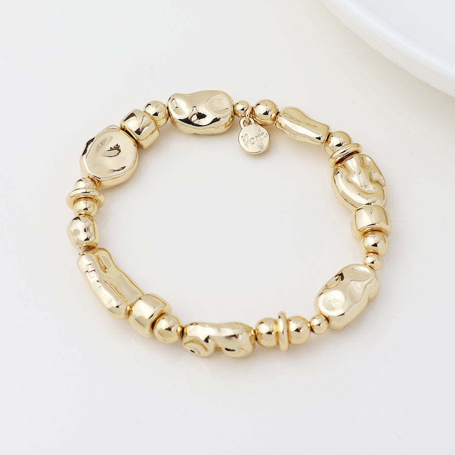 A vegan-friendly gold mixed bead bracelet with irregular, chunky beads and a small round charm, crafted from organic materials and shown on a white surface.