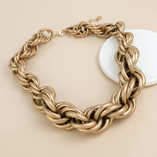 A chunky gold chain necklace with large interlocking links, displayed on a beige surface beside a round white dish, ideal for pairing with your favourite golden mixed bracelet.