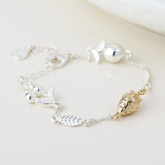 A silver-plated charm bracelet adorned with leaf charms, silver beads, and a gold strawberry fruit charm rests on a white surface—ideal for summer jewellery enthusiasts.