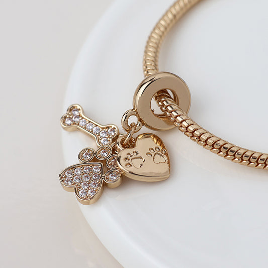 Golden crystals adorn this charm bracelet, ideal for pet lovers, with a crystal-studded bone, paw print heart, and a glittering heart with a paw-shaped cutout displayed on a white surface.