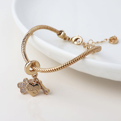 Ideal for animal lovers, this charm bracelet showcases golden crystals on a bear, a heart adorned with paw prints, and a bone, all presented gracefully on a white dish.