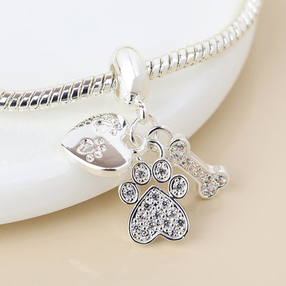 A silver paw charm bracelet with three dangling charms—a heart, a paw print, and a bone—each decorated with sparkling stones. Ideal jewellery for pet owners to wear every day.