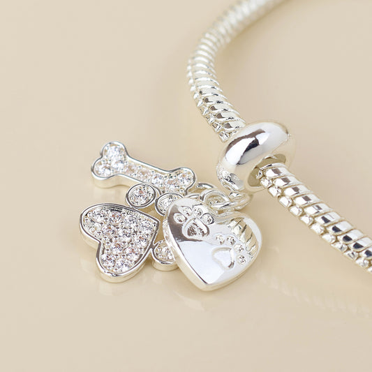 A silver paw charm bracelet featuring three charms—a bone, a heart, and a paw print—embellished with sparkling clear stones. The ideal piece of jewellery for any dog lover or pet parent.