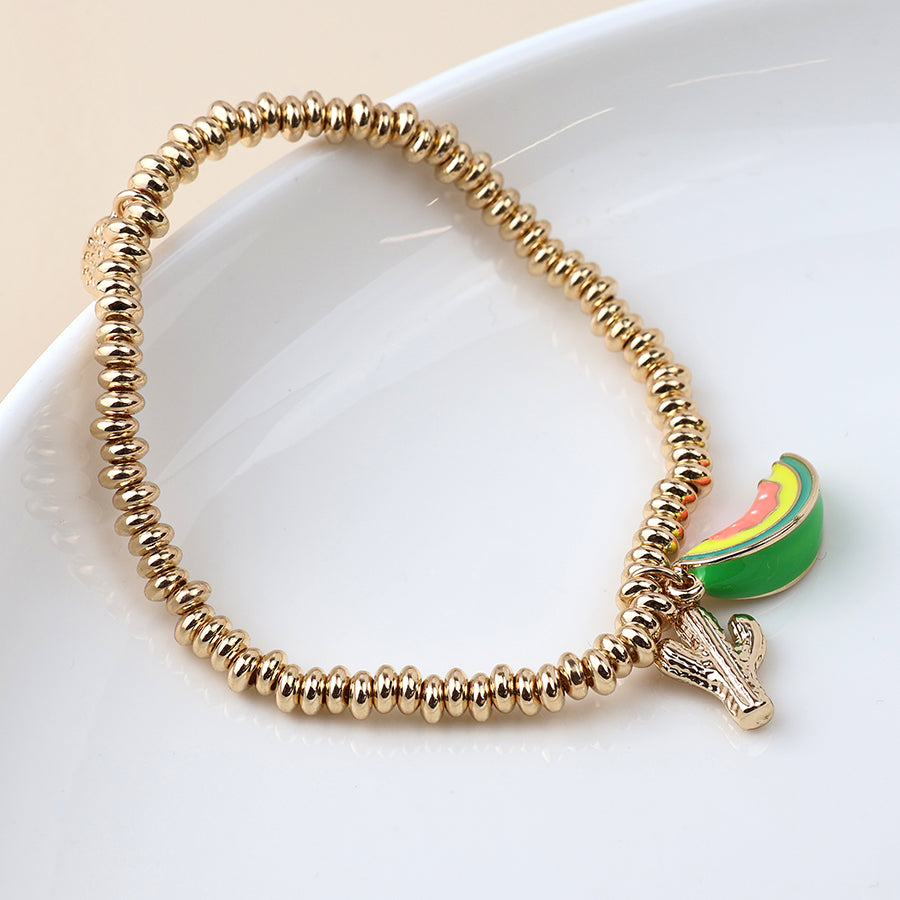 A quirky accessory, this gold beaded charm bracelet features a cactus and watermelon slice charm, shown on a white dish.