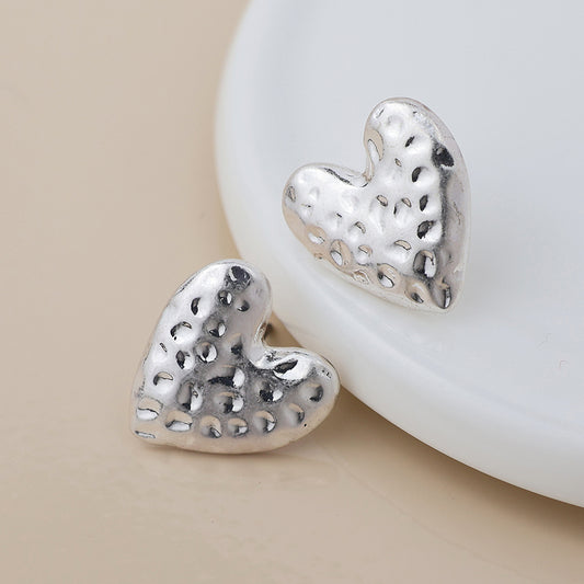 Pair of silver-plated, hammered-texture heart earrings resting on a white ceramic surface.