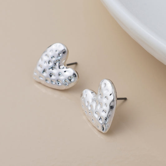 A pair of silver-plated heart earrings with a hammered texture, shown on a light beige background beside a white dish.