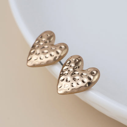 Pair of gold earrings with a hammered finish; these textured heart-shaped earrings bring a touch of elegance, beautifully displayed on a white surface.