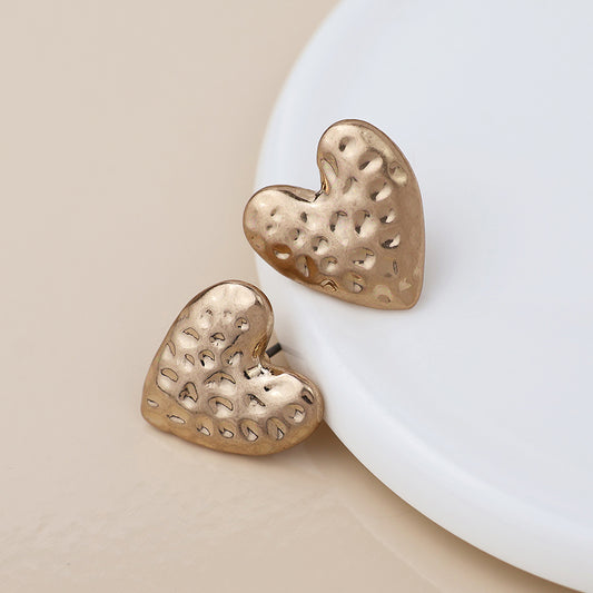 A pair of gold, hammered-finish heart earrings shown on a round white surface.