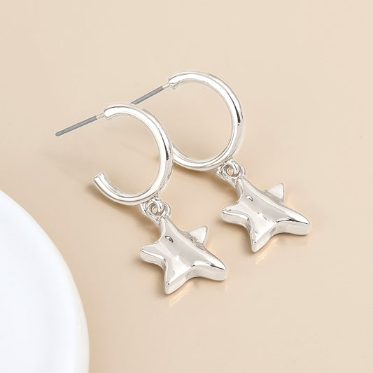 A pair of silver-plated C-hoop earrings with star-shaped pendants shown on a beige surface.
