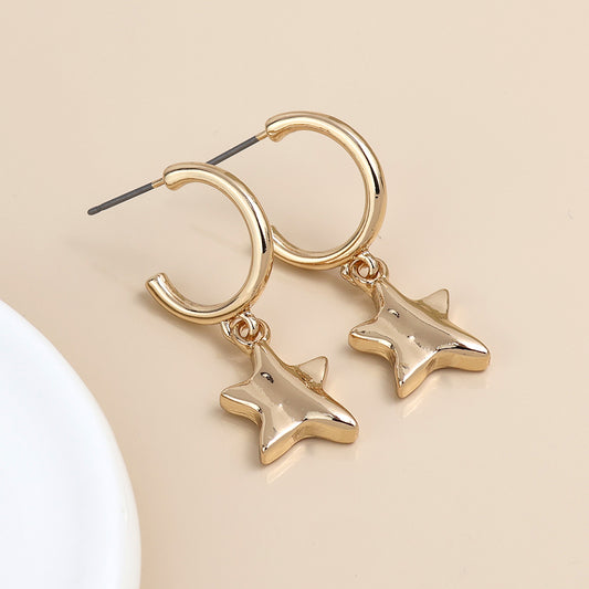 A pair of gold C-hoop earrings with dangling star-shaped charms rests on a beige surface.