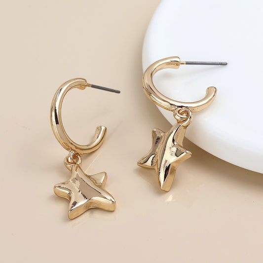 A pair of gold C-hoop earrings with hanging star-shaped charms, displayed on a beige surface.