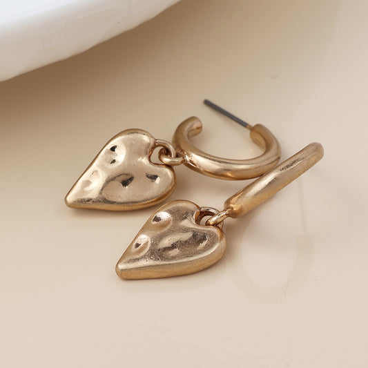 A pair of vintage gold earrings with dangling, textured heart-shaped charms rests on a light beige surface.