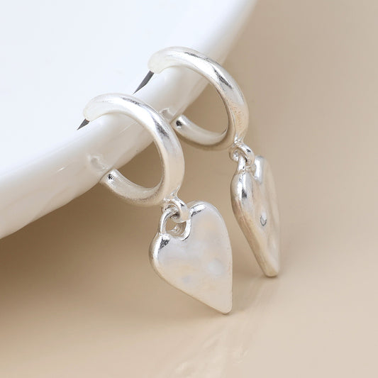 A pair of vintage silver earrings with dangling heart-shaped charms shown on a white surface.