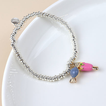 A silver-plated charm bracelet featuring a pink, blue, and gold fish-shaped charm rests on a white plate, ideal for those who appreciate sweet-inspired jewellery.