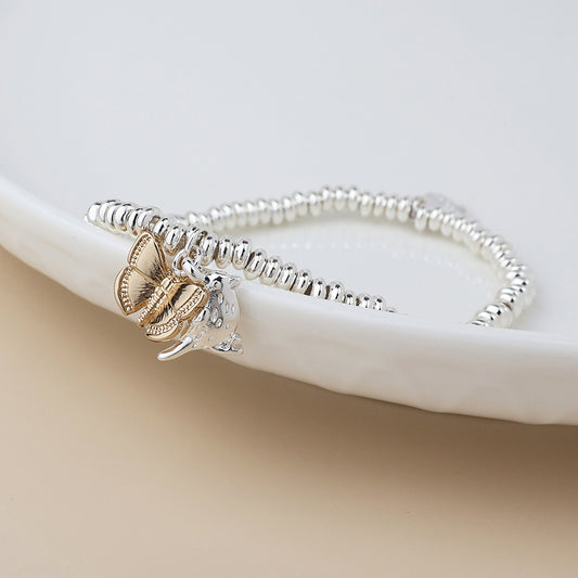 A nature-inspired charm bracelet with silver-plated beads, a gold butterfly, and a leopard head rests elegantly on a white dish.