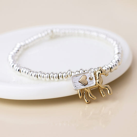 A meaningful jewellery piece, this silver-plated bracelet features gold-toned horse and heart tag charms, stylishly presented on a white ceramic dish.