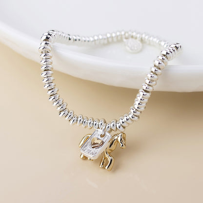 A silver-plated bracelet with a robot charm showcasing gold accents and a heart detail on its chest; this meaningful piece of jewellery is presented on a light surface.