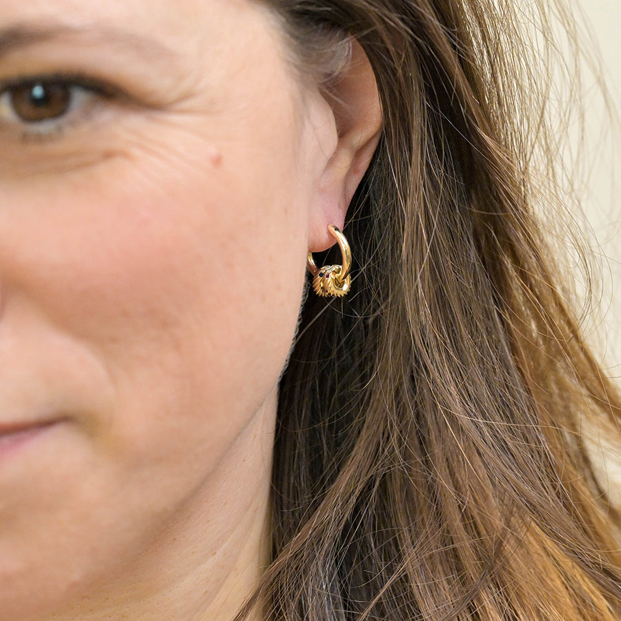 Close-up of a woman's ear adorned with crystal hoop earrings, with part of her face and brown hair visible.
