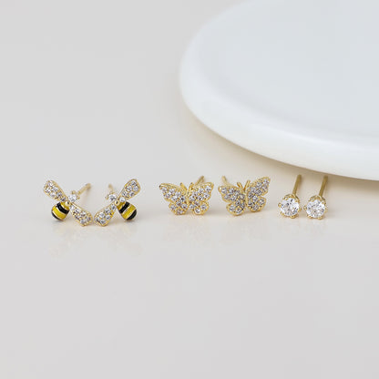 Three pairs of gold earrings are shown: one pair shaped like bees, another with butterfly designs, and a third pair featuring round, crystal stud earrings.