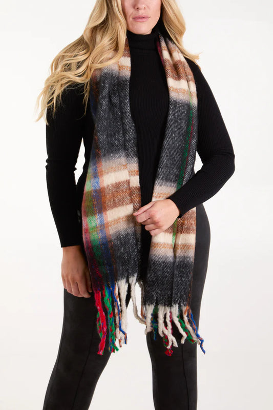 Woman wearing a black polo neck and trousers, with a long tartan scarf featuring fringed ends draped around her neck—a cosy winter accessory for any outfit.