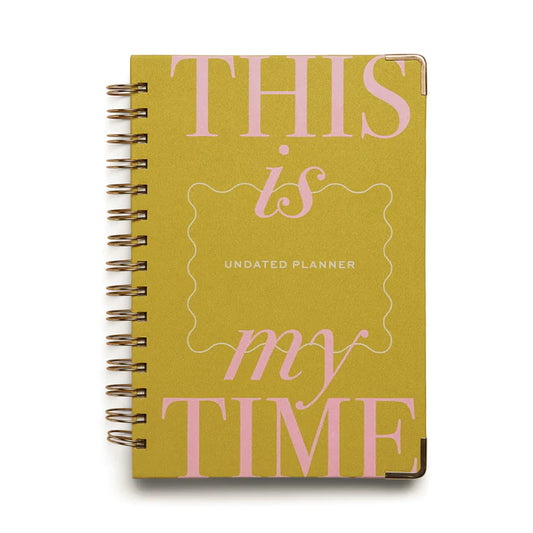 A yellow spiral-bound undated perpetual planner with large pink lettering on the cover that reads THIS is my TIME.