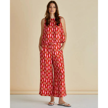 Woman stands against a plain background wearing a sleeveless red patterned top and matching lightweight trousers, hands in pockets, finished with white sandals—an effortless example of ethical fashion.