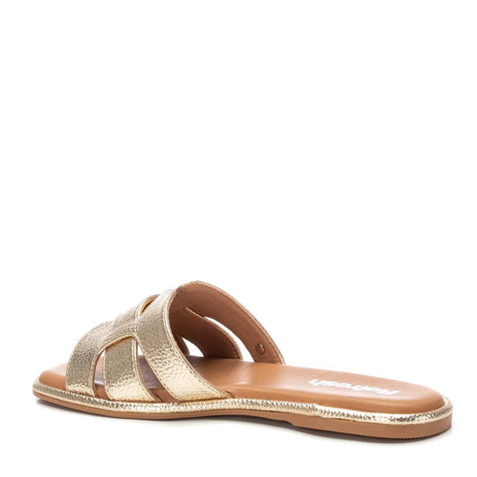 A gold women’s sandal with an open toe, cut-out straps, and a flat sole crafted from premium leather, shown from a rear side angle.