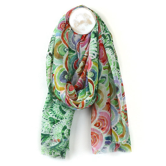 A lightweight scarf made from breathable fabric featuring a colourful, abstract swirl and leaf design in green, red, yellow, and blue, draped over a round wall hook.