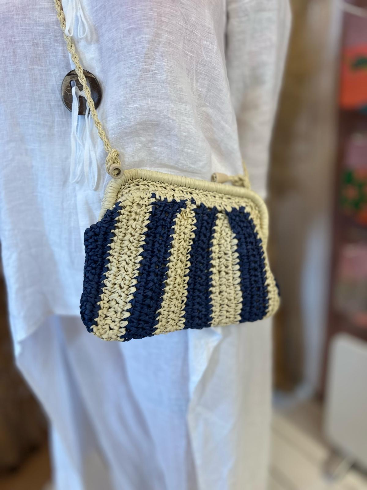 A small, vegan-friendly crocheted shoulder bag with navy blue and beige vertical stripes is worn over a loose, white linen garment.