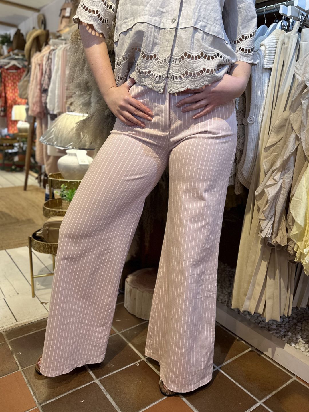 Person wearing high-waisted, pinstripe wide-leg jeans and a lace-trimmed blouse, standing in a clothes shop.