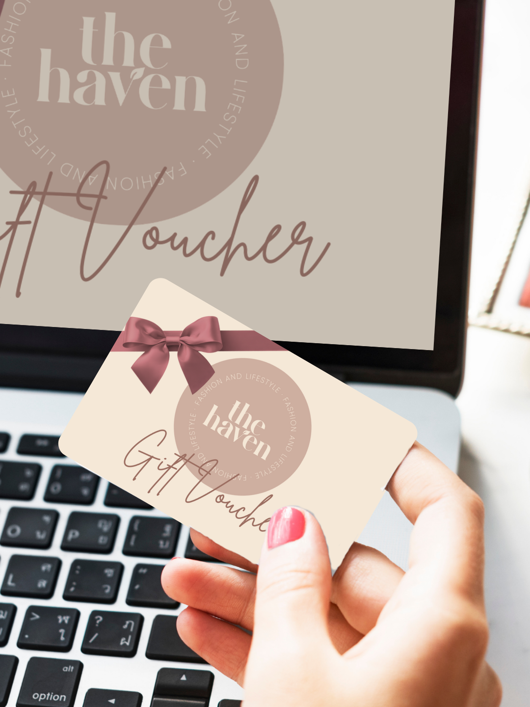 A hand holds a Haven Fashion & Lifestyle e-gift card in front of a laptop showing a matching gift voucher design, ideal for enthusiasts of jewellery and ladies’ clothing.