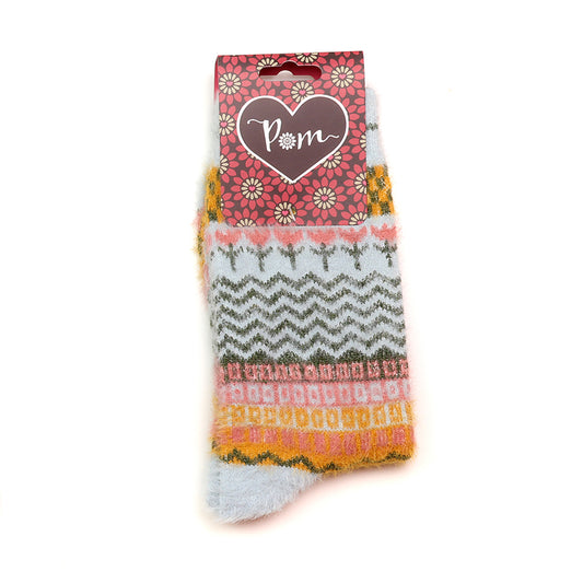 A pair of fluffy vegan socks with multicoloured and pale blue patterns are displayed, featuring a heart-shaped “Pom” label attached at the top.