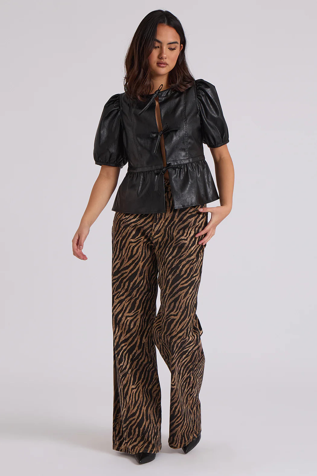 A woman wears a black puff-sleeve top and brown zebra print patterned, high-rise, wide-leg trousers as she stands against a plain background.