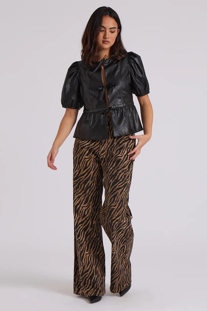 A woman wears a black puff-sleeve top and brown zebra print patterned, high-rise, wide-leg trousers as she stands against a plain background.