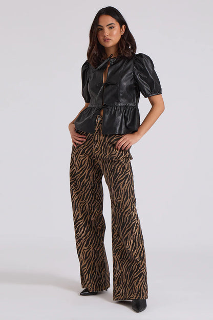 A person in a black leather top with puffed sleeves and zebra wide-leg jeans poses confidently, showcasing the bold zebra print pattern against a plain background.